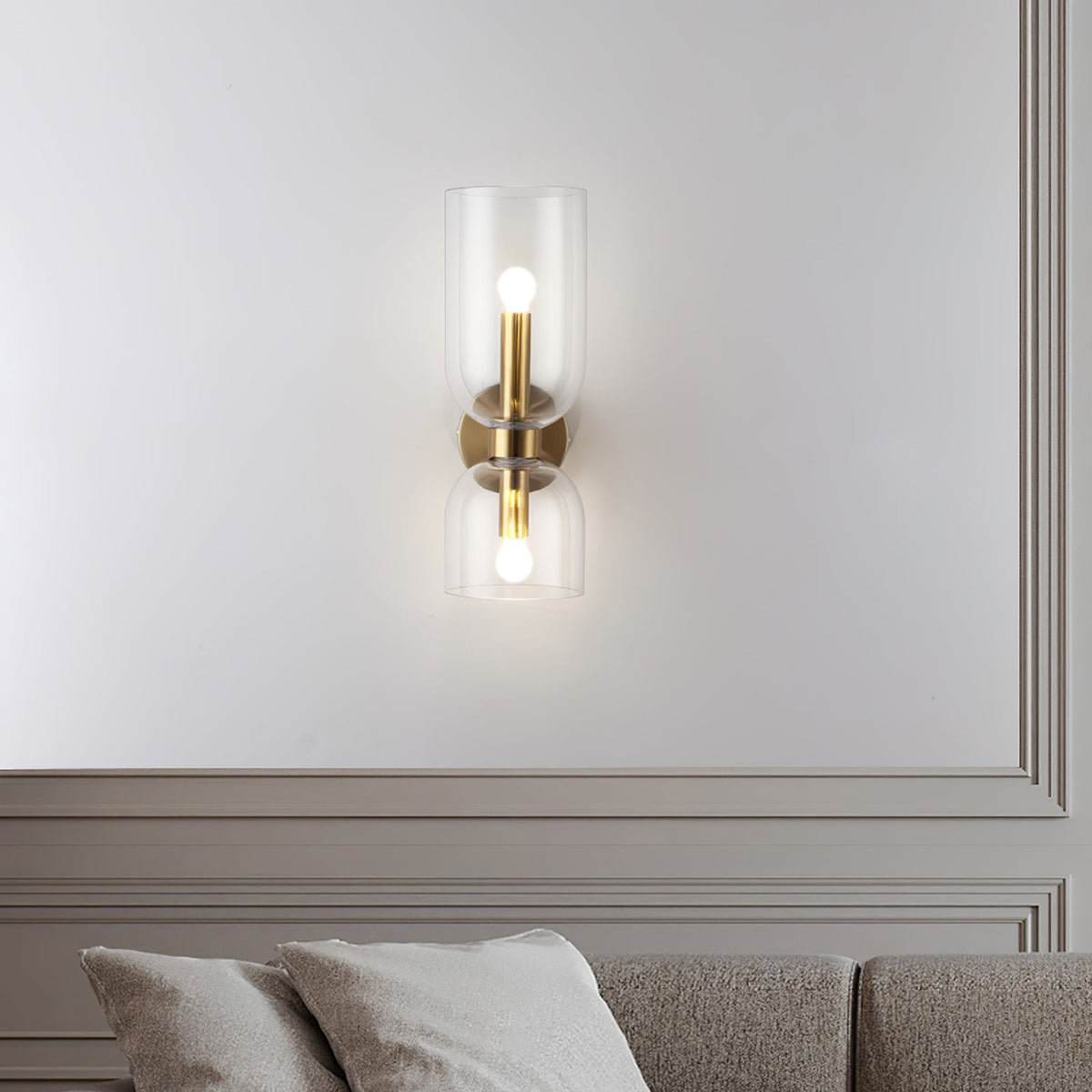 A clear-glass Clérachic sconce in gold lights a panelled wall above cushions in this living room.