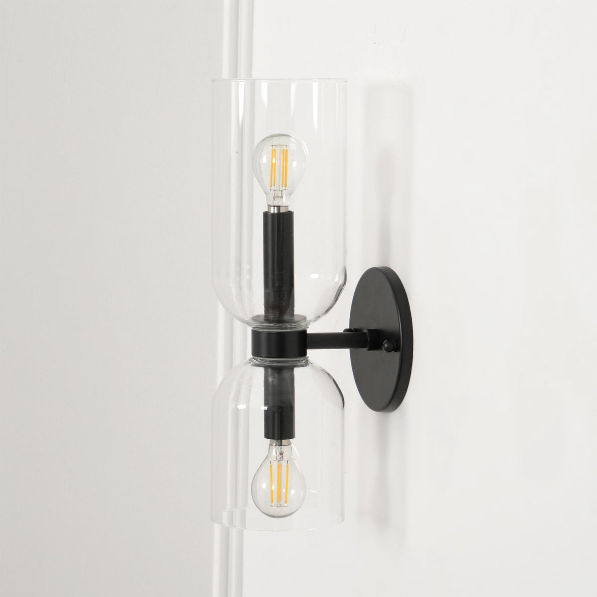 A narrow view shows the cord and clear glass shades of this matt black Clérachic wall light, lit.