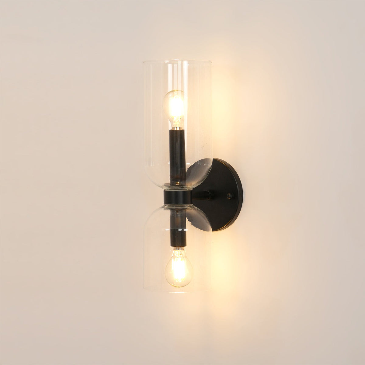 Warm light glows through the clear glass cylinders of this matt black Clérachic sconce.