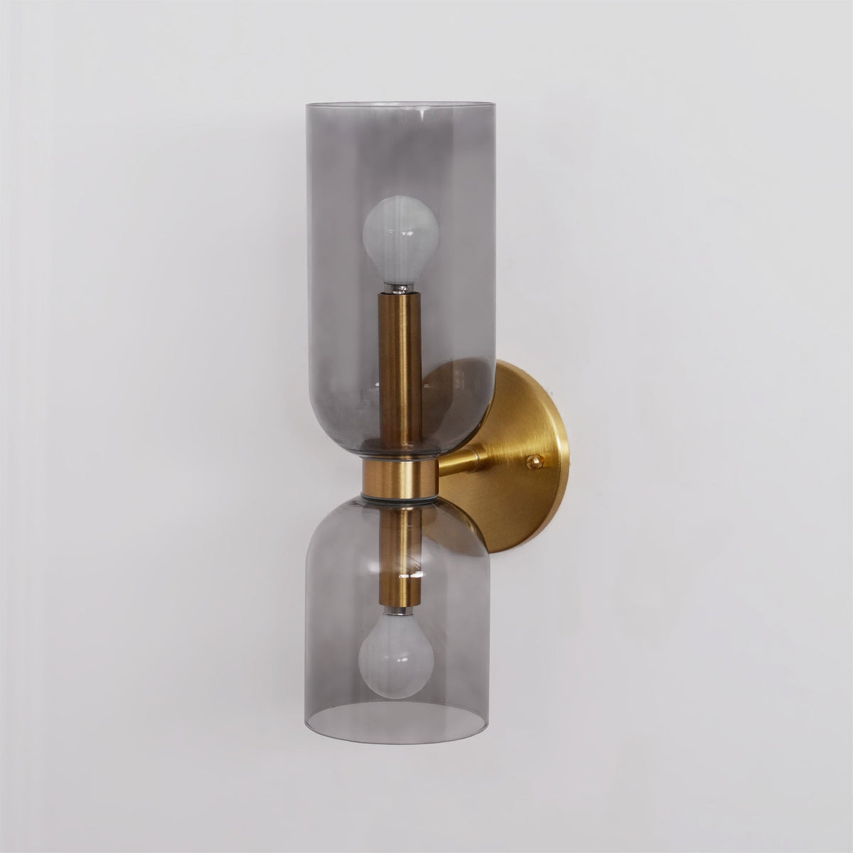 Angled against white, this gold Clérachic wall light's smoke grey shades glow around the bulbs.