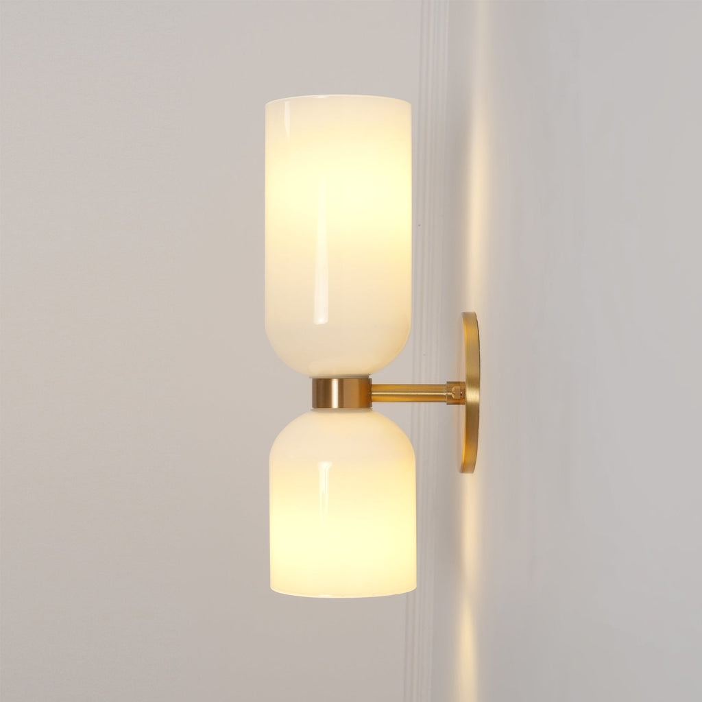 In gold, this Clérachic sconce pairs opal glass shades that glow warmly on a soft grey-beige wall.