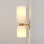 In gold, this Clérachic sconce pairs opal glass shades that glow warmly on a soft grey-beige wall.