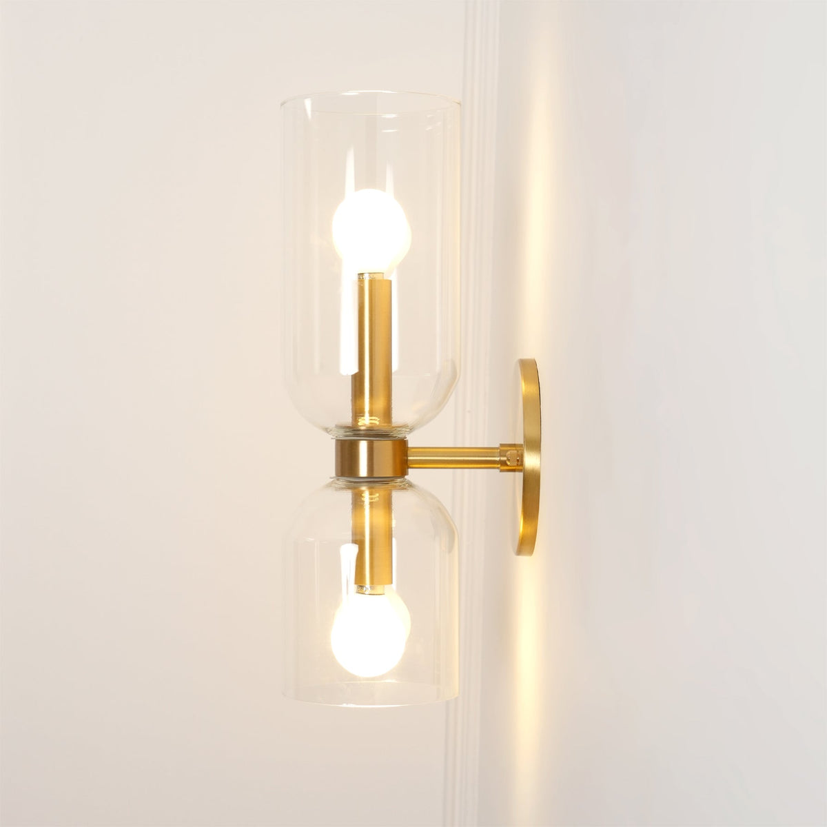 Warm light spills onto the wall from this gold Clérachic wall light's clear glass shades.