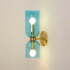 Warm light fills the blue glass shades of this gold Clérachic sconce on a cream wall.