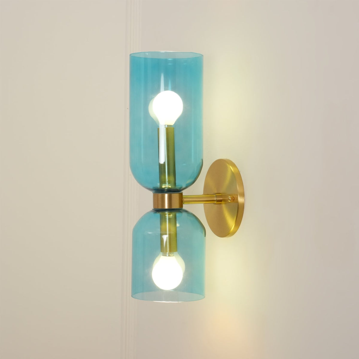 Warm light fills the blue glass shades of this gold Clérachic sconce on a cream wall.