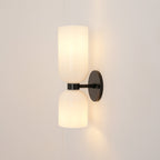 This Clérachic wall sconce in matt black holds two opal glass shades glowing softly against a warm taupe wall.