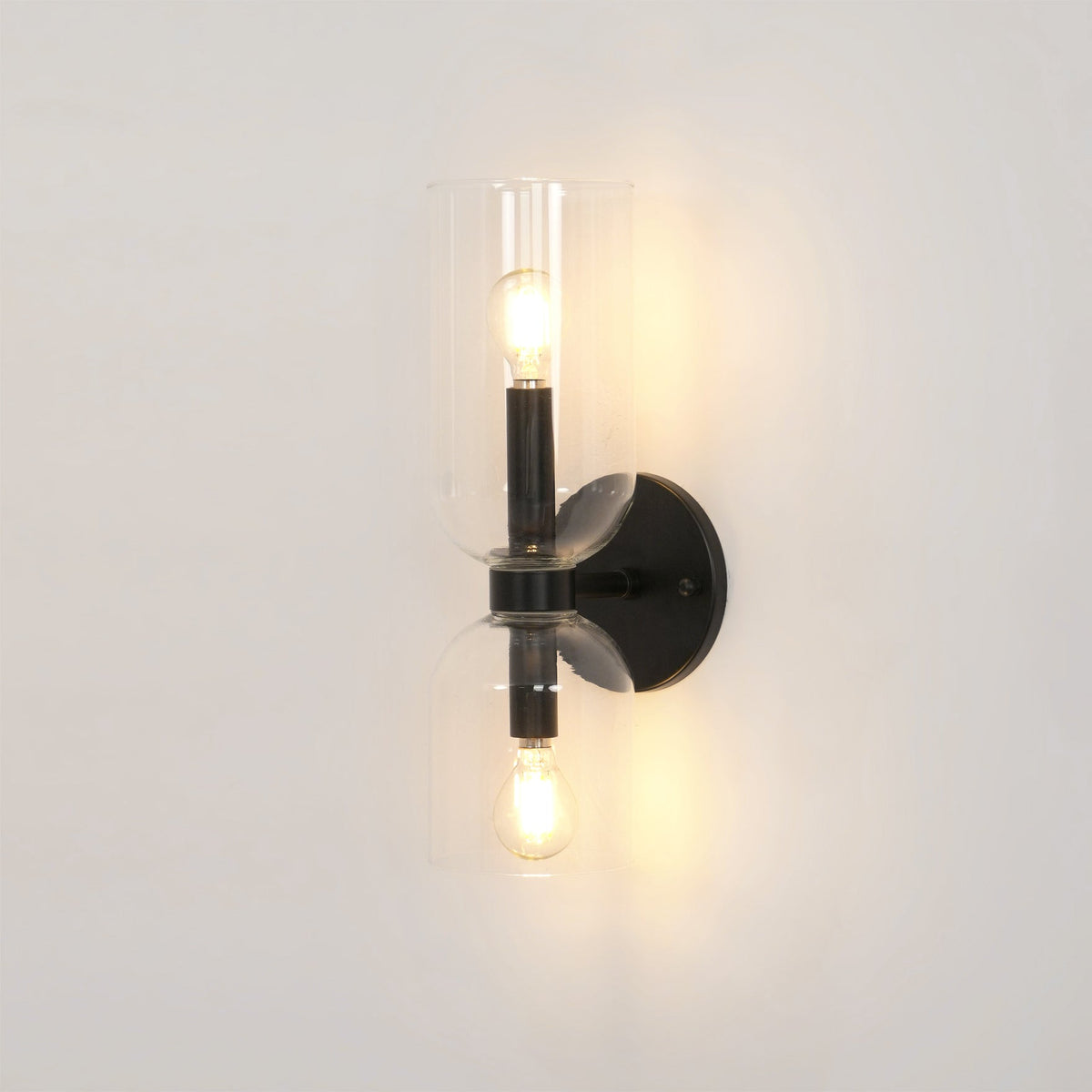 A close view of this matt black Clérachic wall light shows its clear glass shade lit from within.