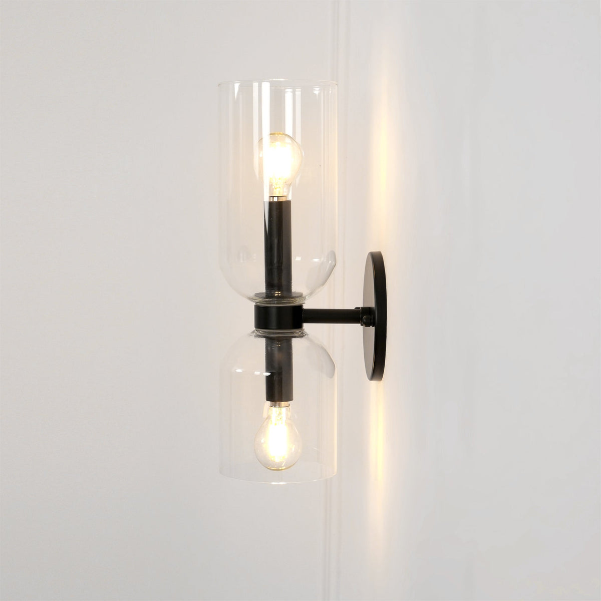 Set on a cream wall, this matt black Clérachic sconce's clear glass cylinders glow around each bulb.