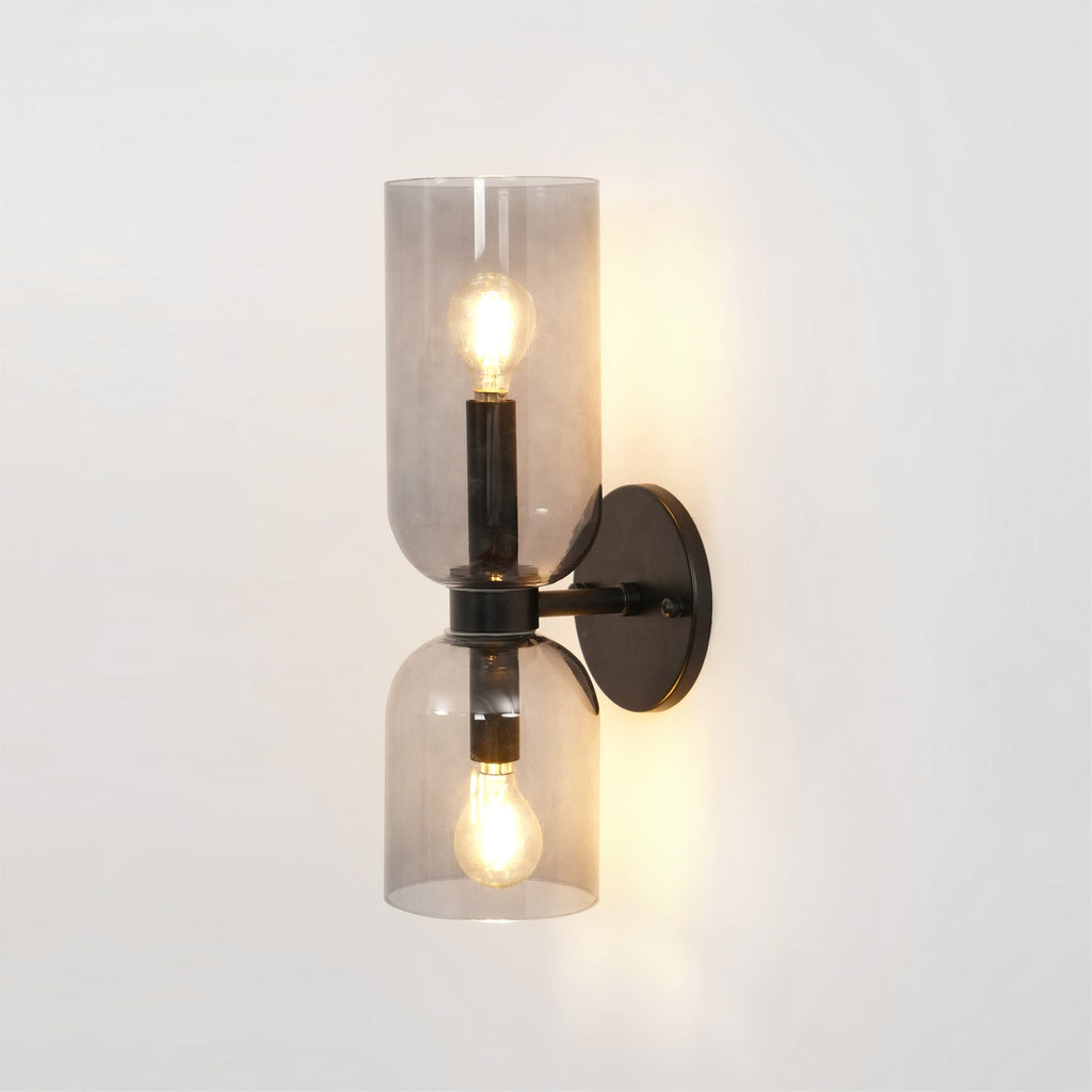 Smoke grey glass wraps the lit bulbs of this matt black Clérachic sconce on a white wall.
