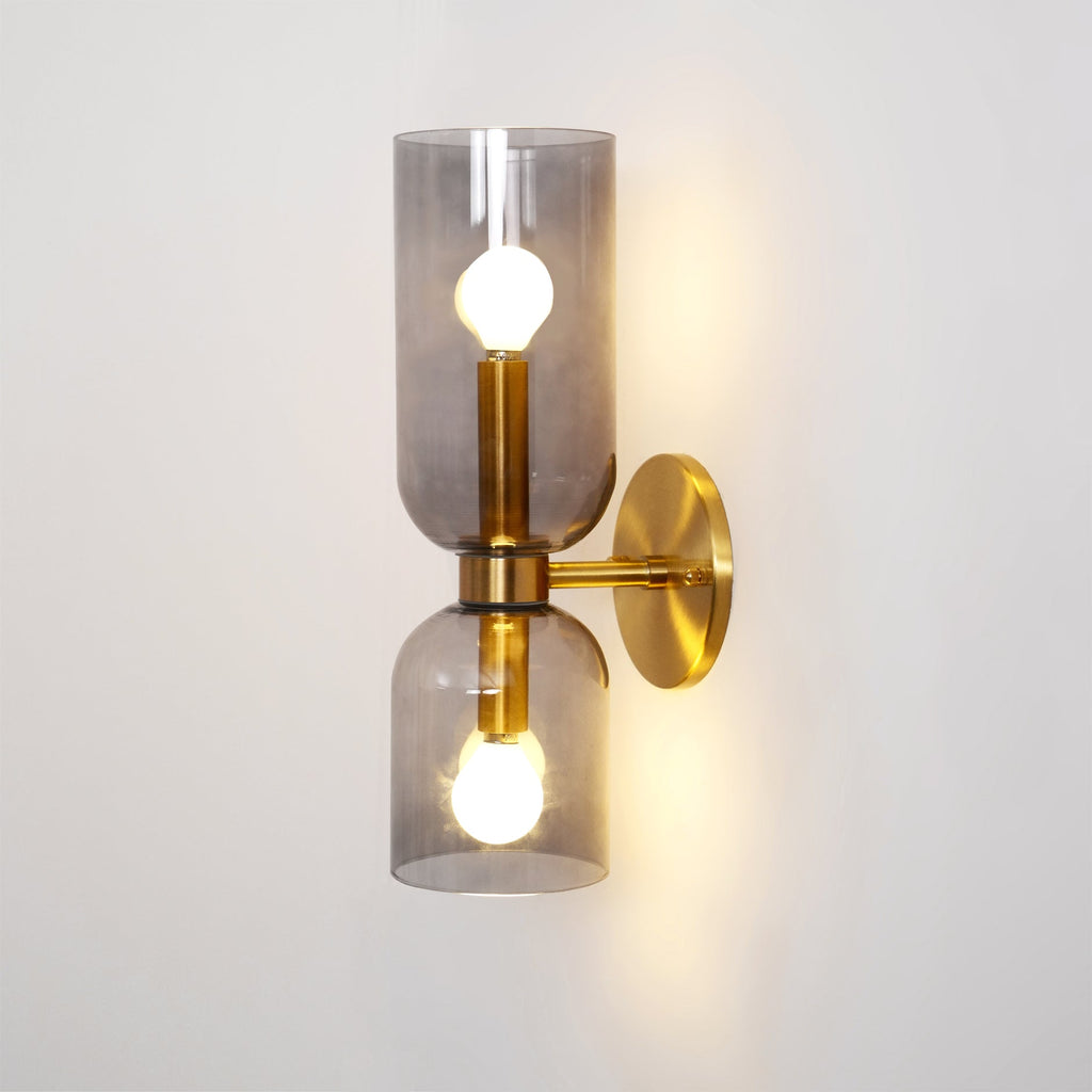 On a warm beige wall, this gold Clérachic sconce's smoke grey glass shades glow softly.
