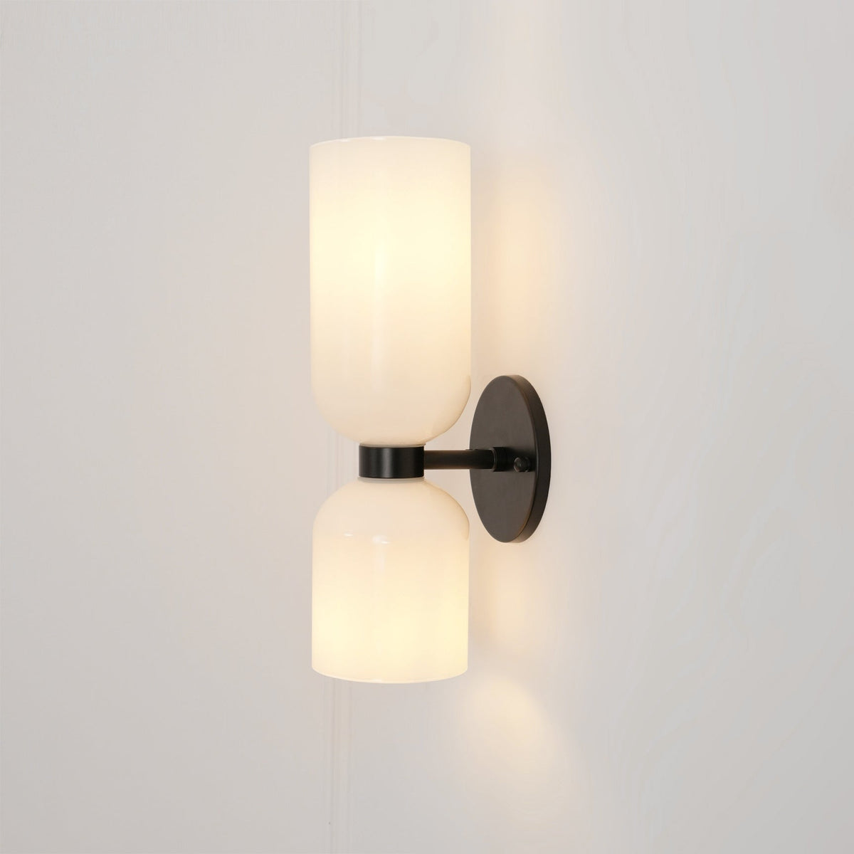 Unlit, the two opal glass shades of this matt black Clérachic sconce sit against a pale taupe wall.