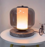 The Clérachic table lamp lit on its round table, shown from a slightly lower angle with the toy bicycle beside it.