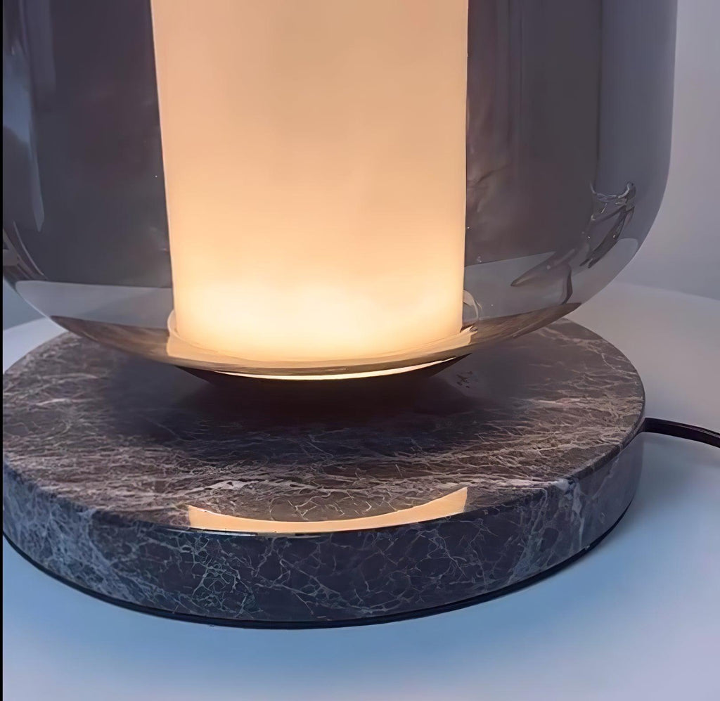 Extreme close-up of the Clérachic table lamp's dark marble base, its veined texture lit by the warm glow above.