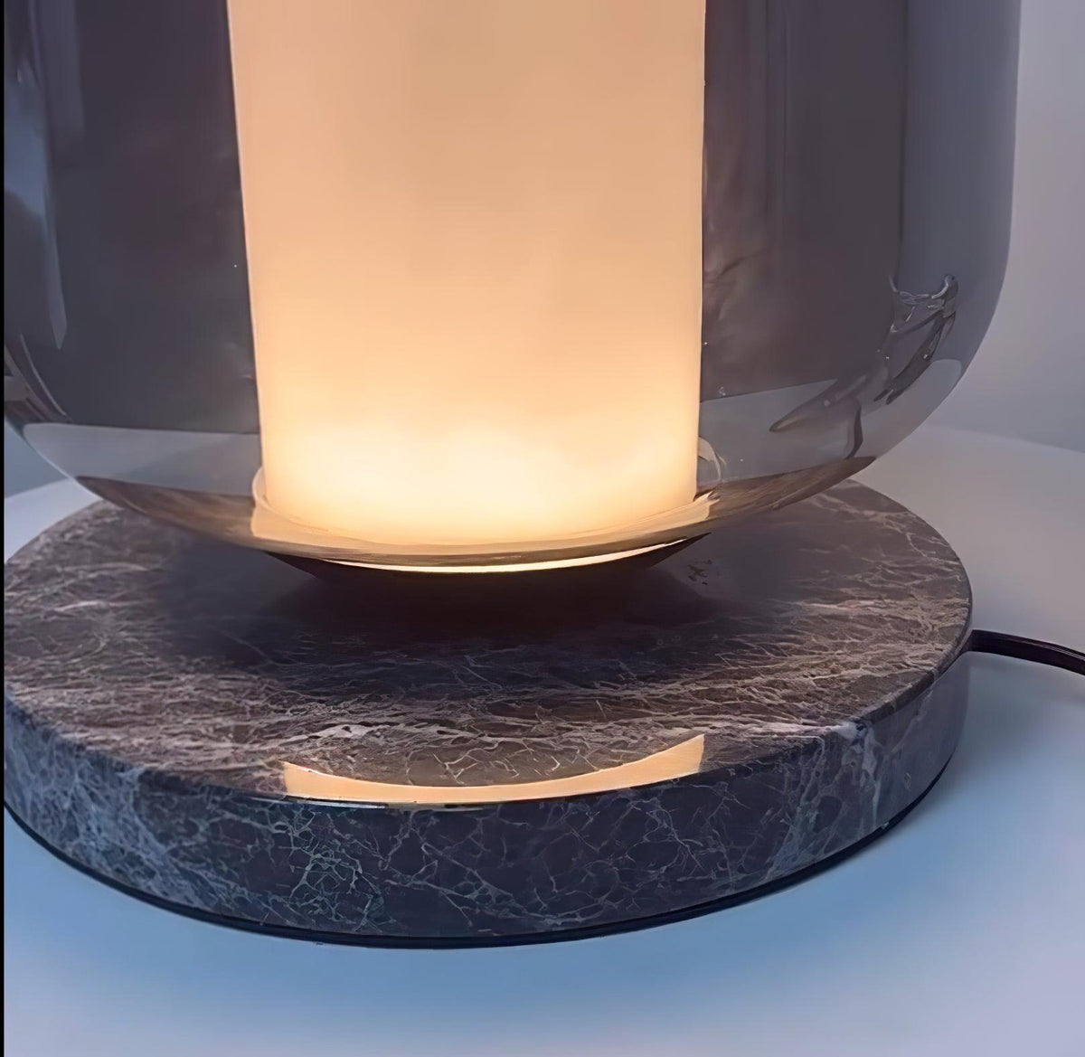 Extreme close-up of the Clérachic table lamp's dark marble base, its veined texture lit by the warm glow above.