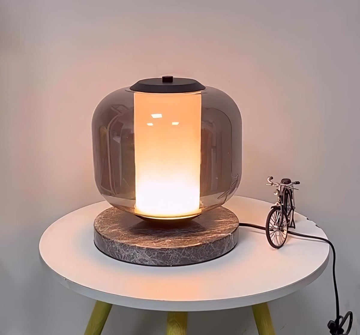 A wider view of the Clérachic table lamp on its round table, the yellow stand legs and toy bicycle visible in frame.