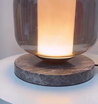 Close-up of the Clérachic table lamp's marble base with the warm light spilling down from the glass shade above it.