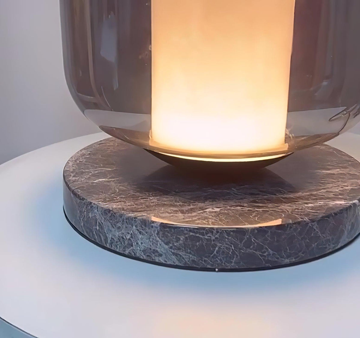 Cropped close-up on the Clérachic table lamp's marble base texture, warm light glowing in the glass shade above it.