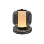 A small full product shot of the Clérachic table lamp glowing warm amber, isolated against a plain grey background.