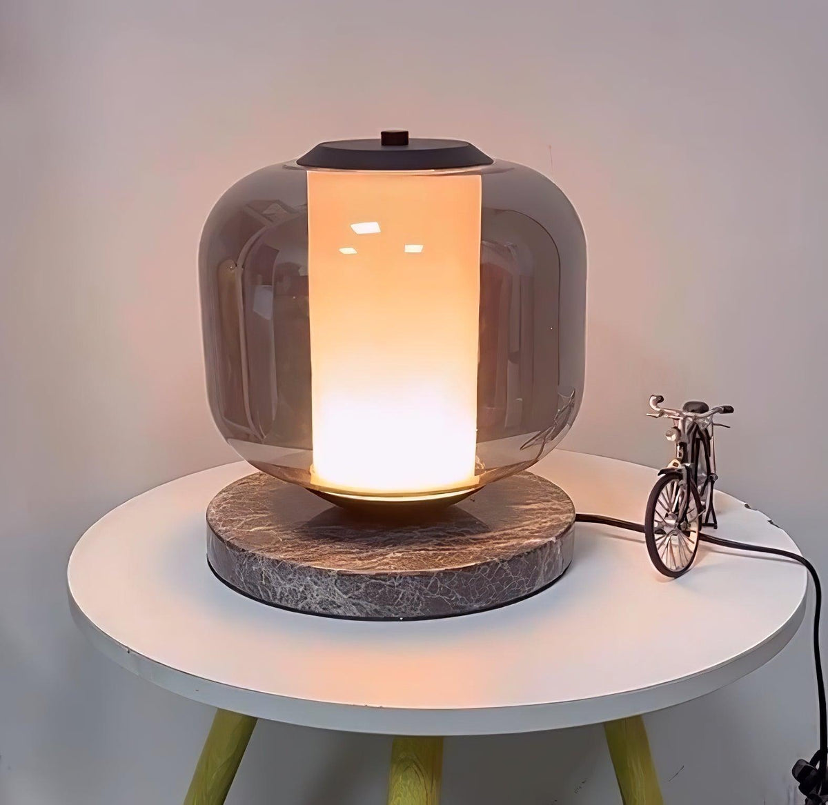 The Clérachic table lamp glows warmly on its bedside table, with the toy bicycle prop and power cord visible beside it.