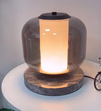 Close-up of the Clérachic table lamp's smoke-grey glass dome, cropped tight to show the glowing column and marble rim.