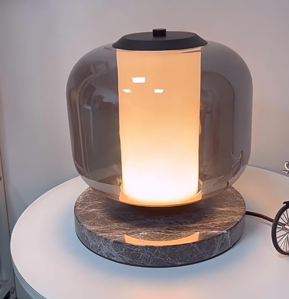 Another close crop of the Clérachic table lamp's glass shade, the warm light glowing brighter through its lower half.