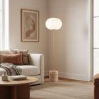 The Clérachic floor lamp lights a minimal corner beside a beige sofa with terracotta and rust-toned cushions.