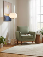 A sunlit reading corner pairs the Clérachic floor lamp with a sage green armchair and a round wooden side table.