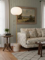 The Clérachic floor lamp glows beside a floral-print sofa against a sage green tongue-and-groove wall.