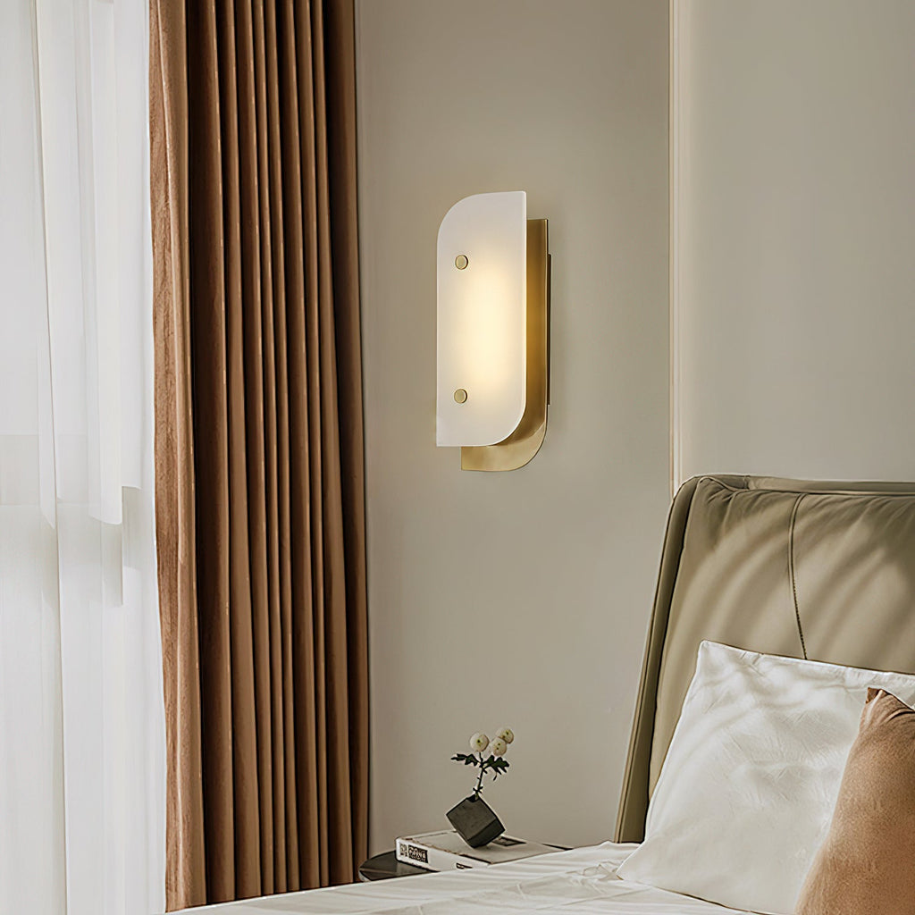 Short Elaris Alabaster Wall Light in brass by a curtained bedroom window, lit above a small nightstand.