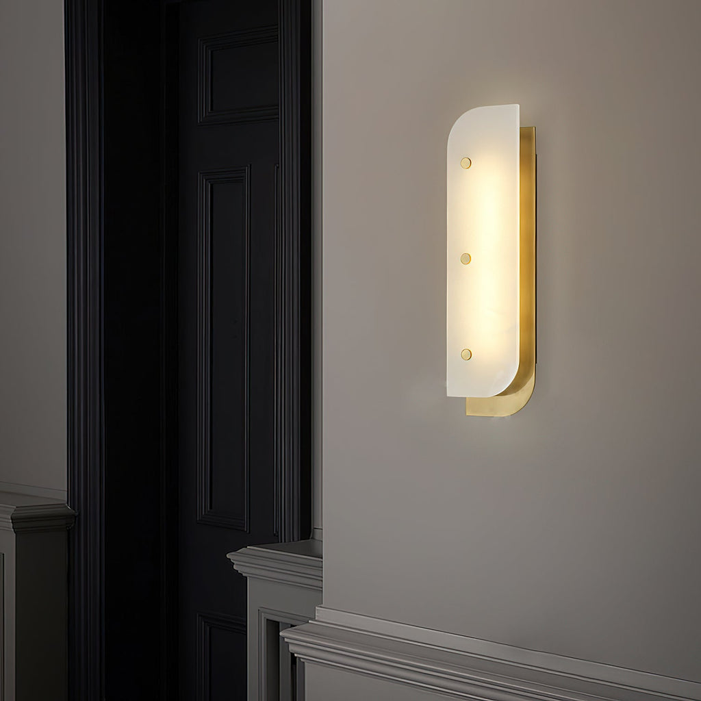 Tall Elaris Alabaster Wall Light in brass beside a black panelled door, lighting a hallway at night.