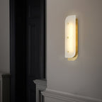 Tall Elaris Alabaster Wall Light in brass beside a black panelled door, lighting a hallway at night.