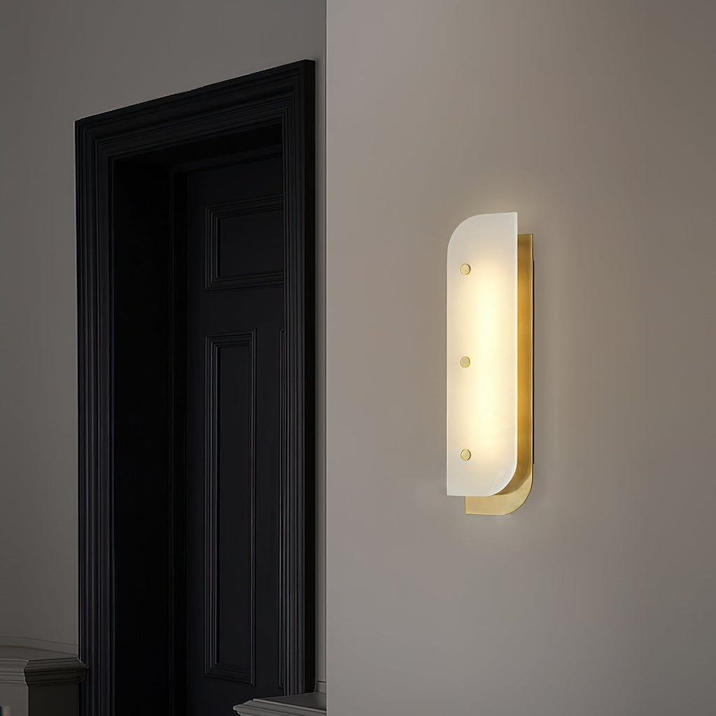 Tall Elaris Alabaster Wall Light in brass on an entry wall, glow spilling onto the dark panelled door.