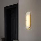 Tall Elaris Alabaster Wall Light in brass on an entry wall, glow spilling onto the dark panelled door.