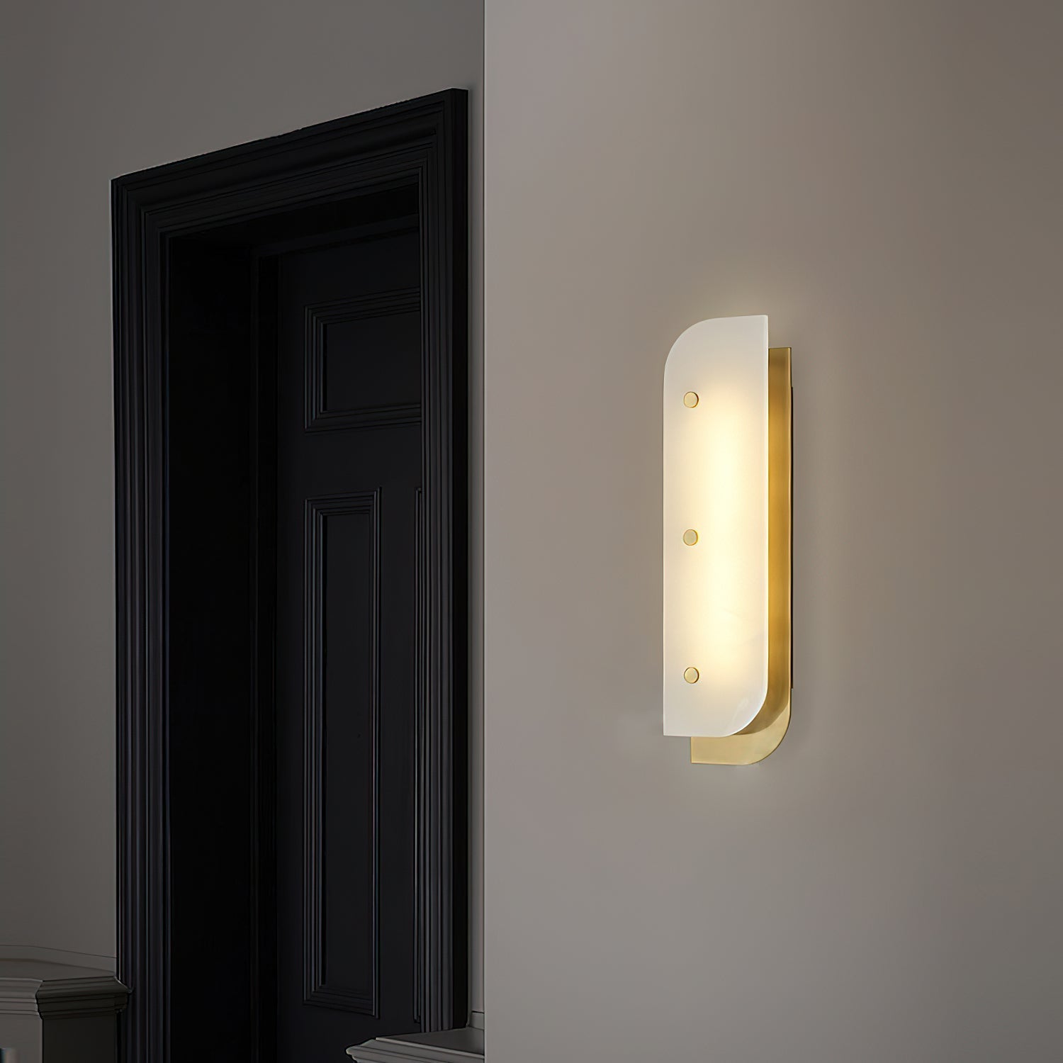 Tall Elaris Alabaster Wall Light in brass on an entry wall, glow spilling onto the dark panelled door.