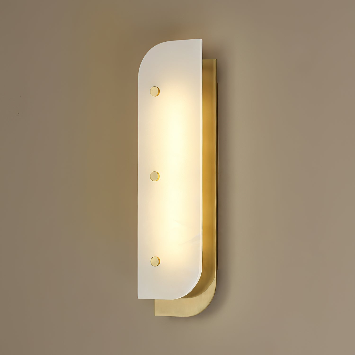 Tall Elaris Alabaster Wall Light in brass lit on a taupe wall, three studs spaced down the stone face.