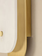 Close-up of the Elaris wall light's brushed brass backplate curving away from the stone panel on a plaster wall.