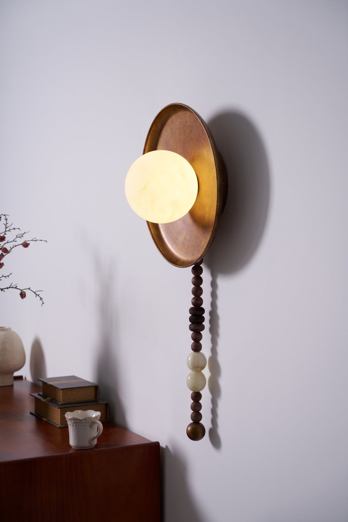 From another angle, the Clérachic sconce's shade projects forward above a dresser dressed with books and a vase.