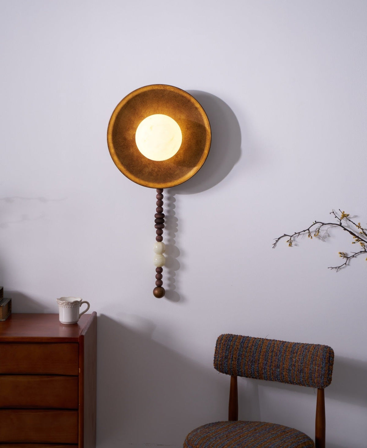 Angled and lit, this close crop of the Clérachic sconce takes in the dresser edge, a cup and a chair alongside.