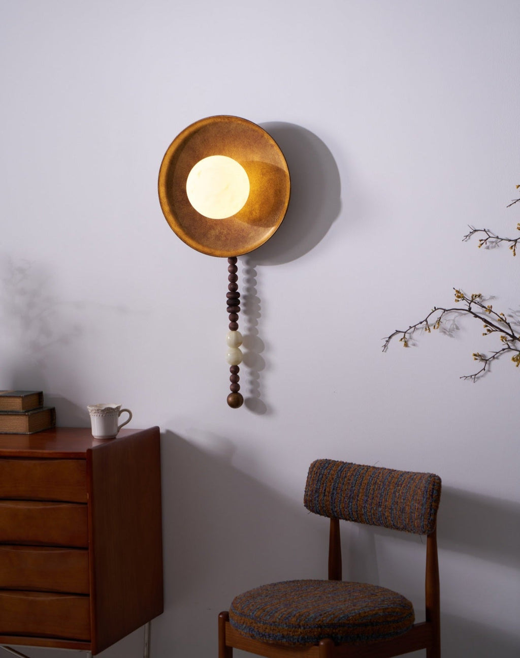 Framed tightly with a chair in view, the lit Clérachic sconce hangs above the dresser's books and cup.