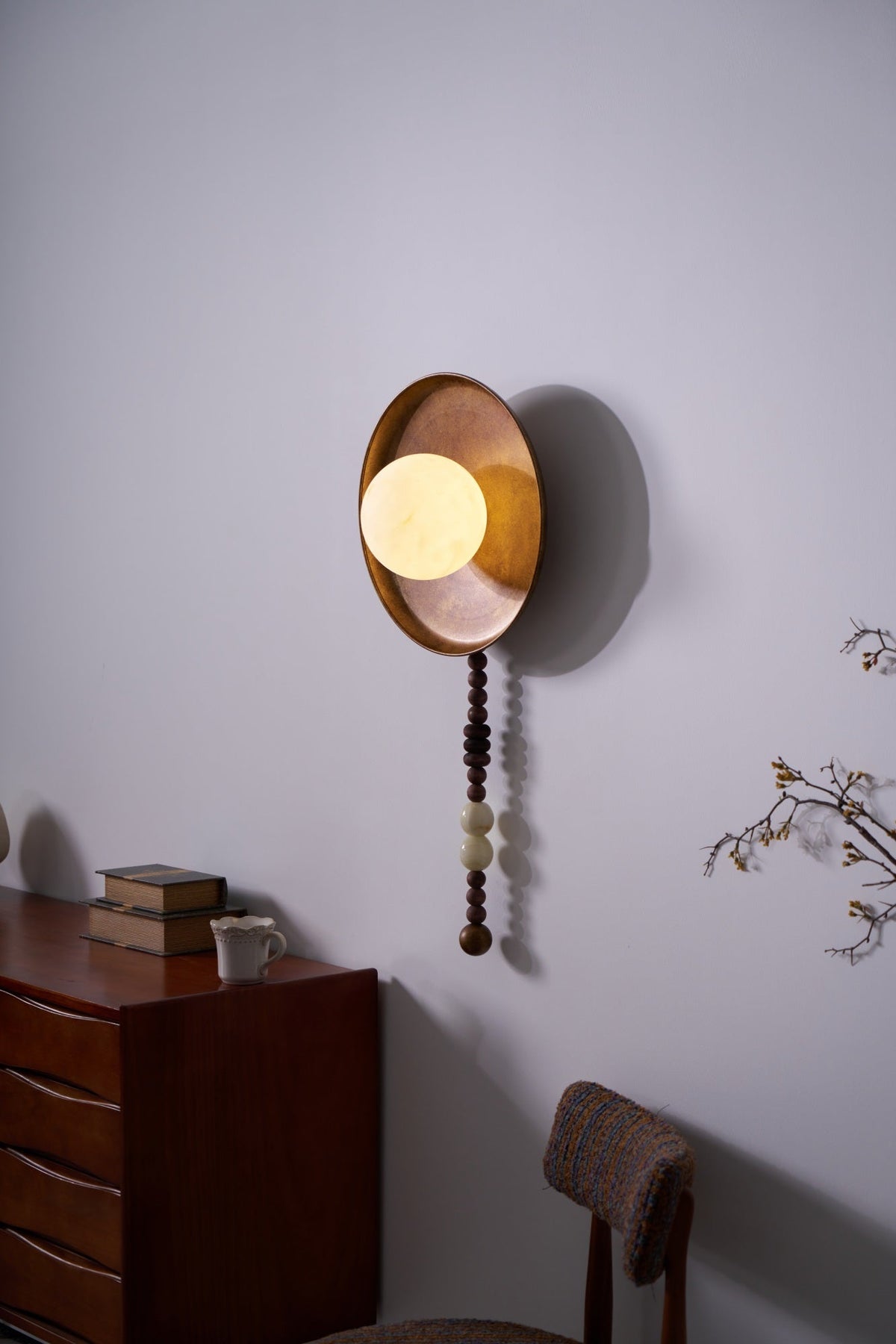 In a darker, evening-styled room, the Clérachic sconce's shade glows warmly above the dresser and its branch.