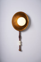 Lit and centred on white, the Clérachic sconce shows its warm glow against the burnished brass-tone dish.