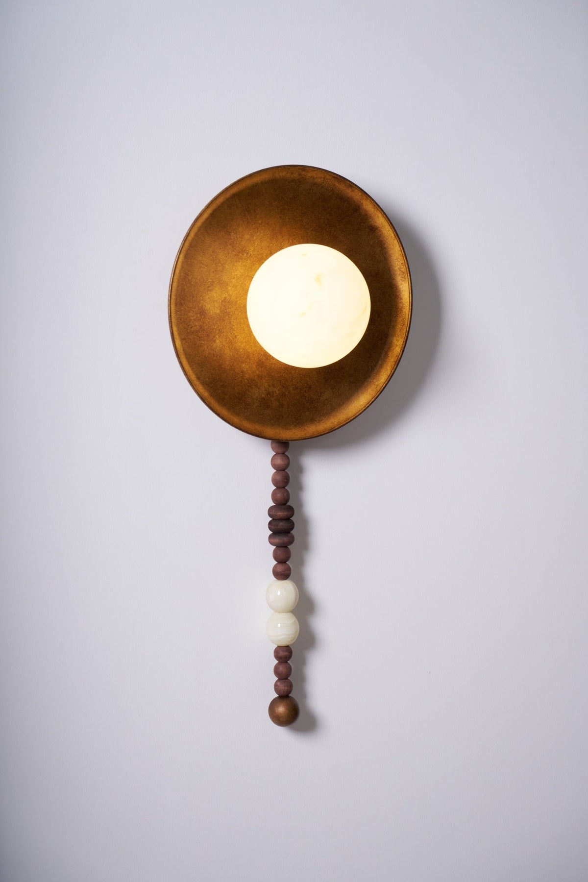 Lit and centred on white, the Clérachic sconce shows its warm glow against the burnished brass-tone dish.