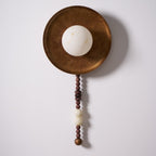 On white with the bulb off, this close view highlights the texture of the Clérachic sconce's disc and beads.