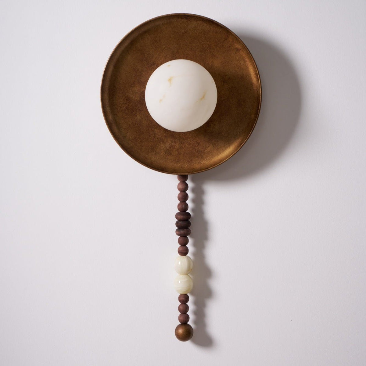 On white with the bulb off, this close view highlights the texture of the Clérachic sconce's disc and beads.