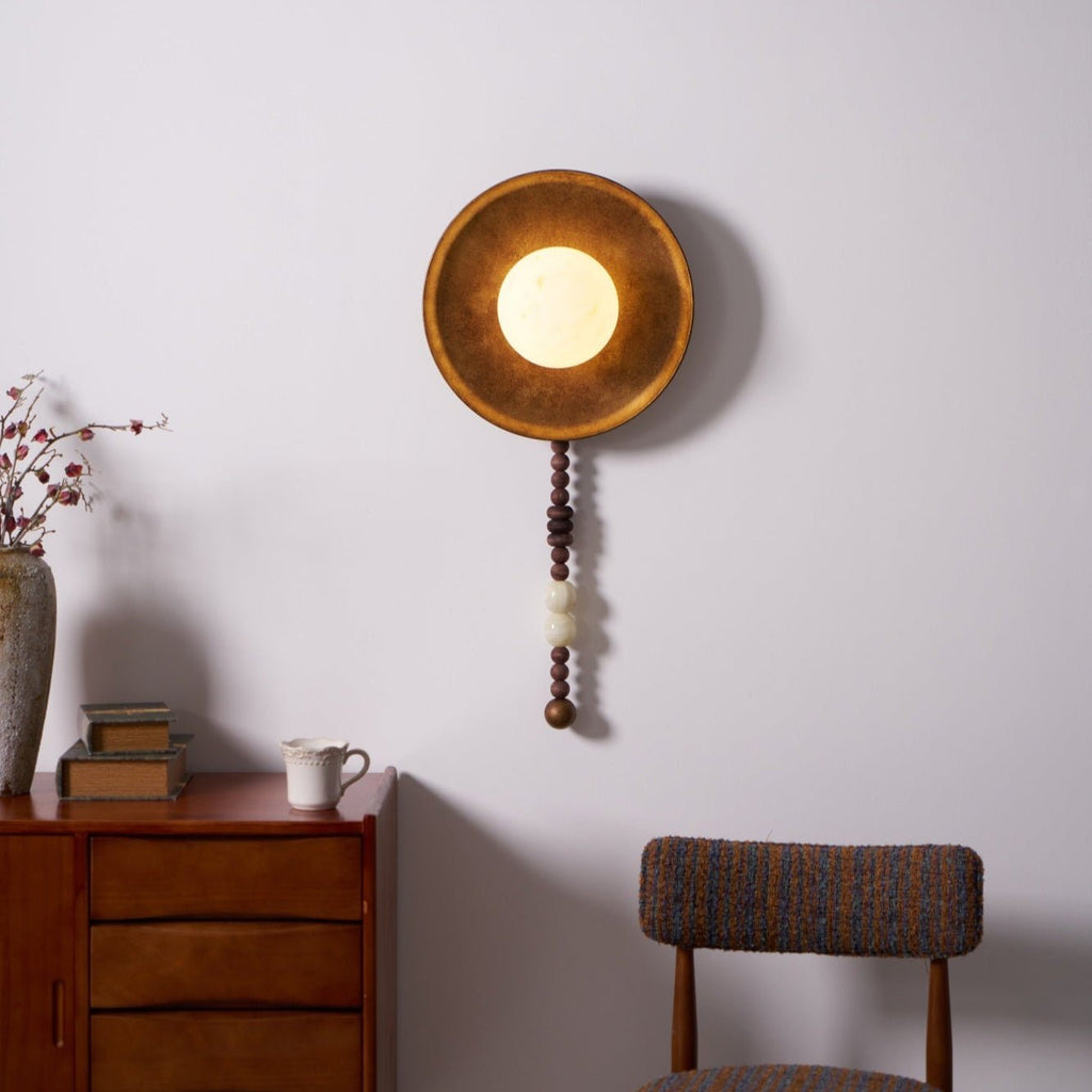 The Clérachic sconce glows above a dresser styled with dried flowers in a vase, books and a chair nearby.