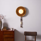 The Clérachic sconce glows above a dresser styled with dried flowers in a vase, books and a chair nearby.