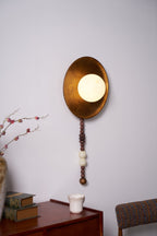A slender branch sits beside the lit Clérachic sconce, mounted above the same dresser with its books and cup.