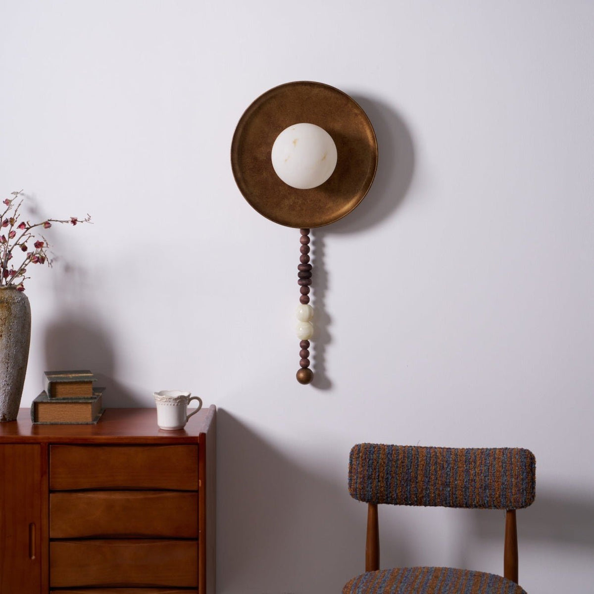 The wood and marble bead drop hangs fully visible on this Clérachic sconce, styled above the dresser's books.