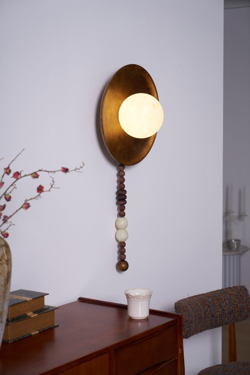With a doorway visible beyond, the lit Clérachic sconce brightens a bedroom corner set with candlesticks and books.