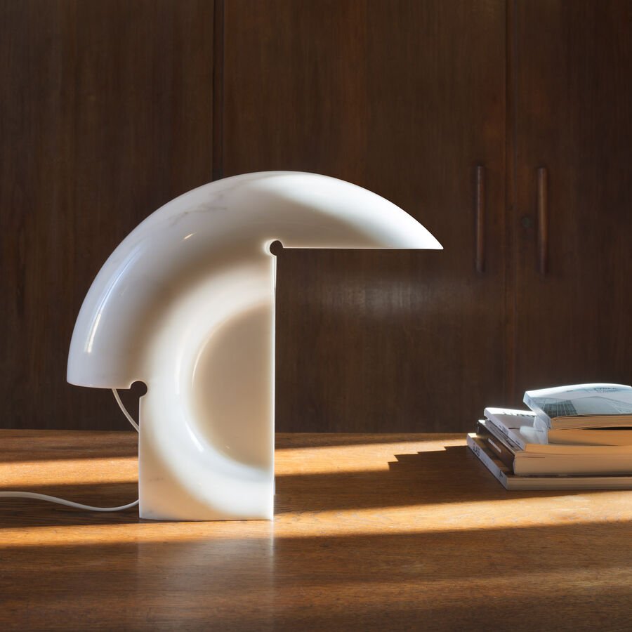 Clérachic resin crescent lamp glowing on a wood table against dark cabinet doors, its cord trailing across the sunlit surface.